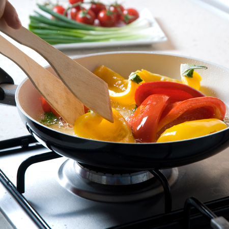 Cuisson des poivrons rouges et jaunes dans une casserole sur un élément de la cuisinière au propane.