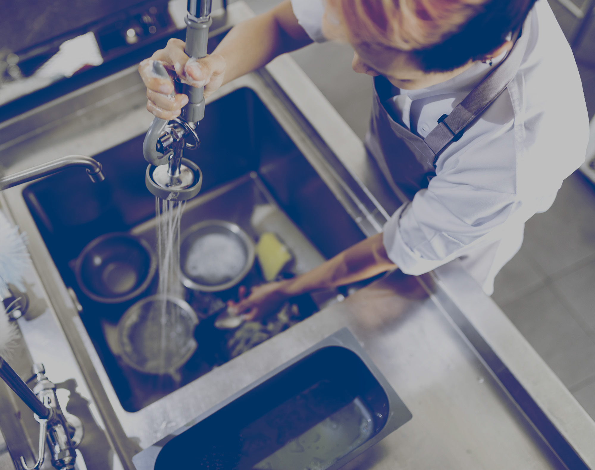 Un plongeur dans la cuisine d’un restaurant rince de la vaisselle sale dans un évier dont l’eau est chauffée au propane.