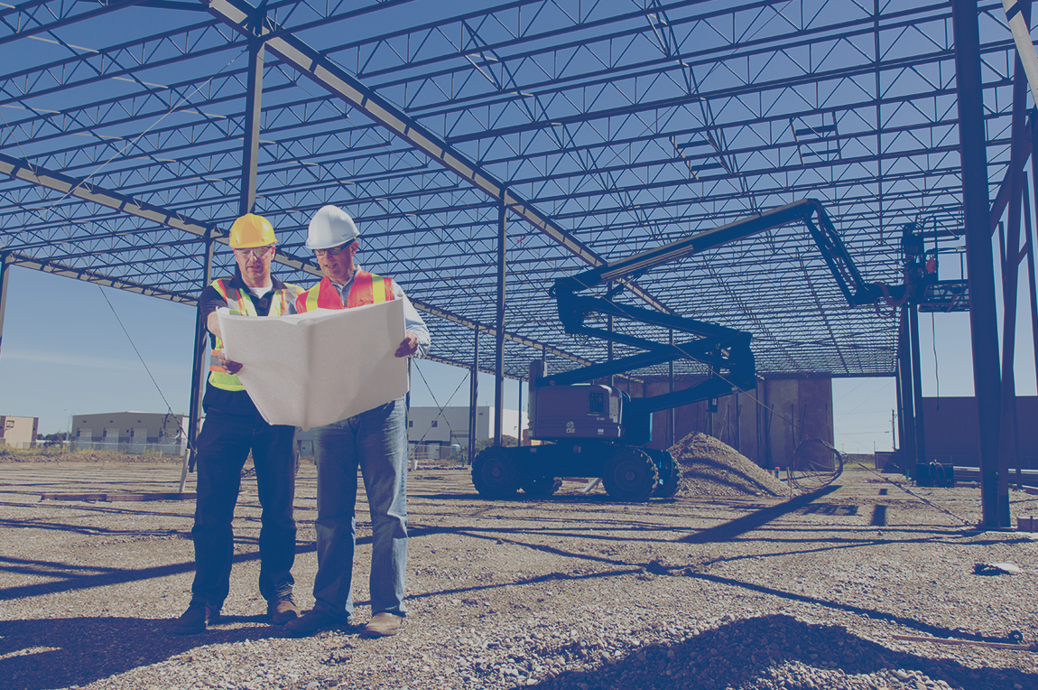 Deux ingénieurs examinent des plans dans un immeuble industriel en construction.