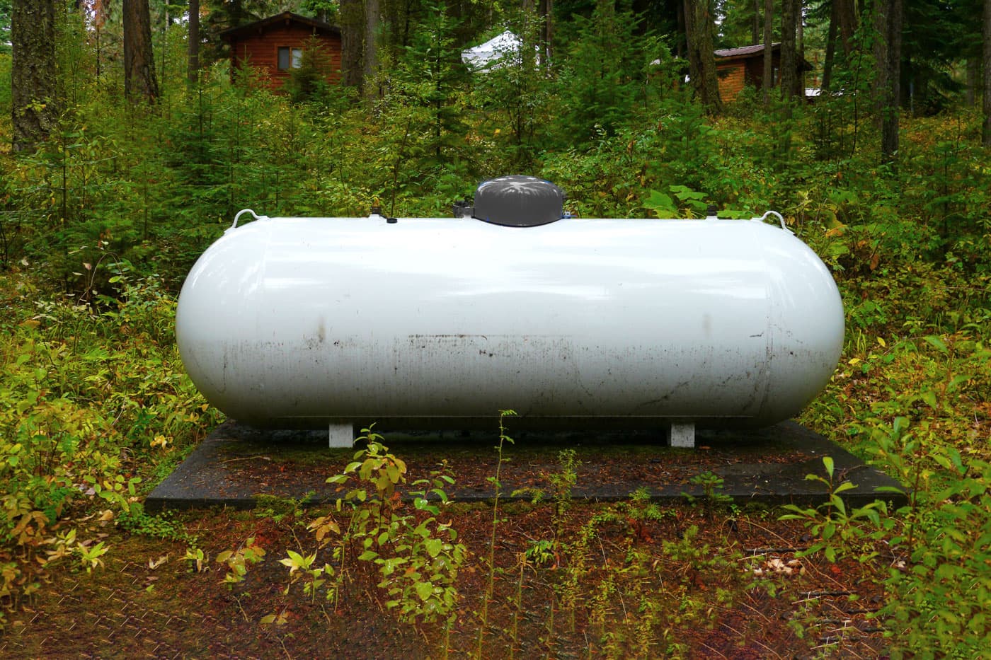 Réservoir au propane blanc dans un espace boisé, près d'une maison.