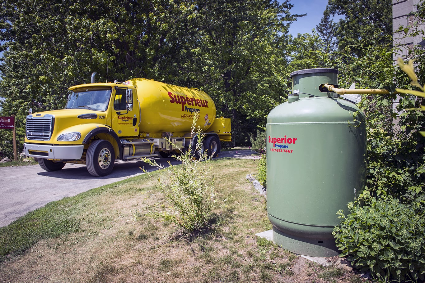 Un camion jaune de Supérieur Propane est garé sur le bord d'une route, un réservoir vert de 420 livres de propane se trouve au premier plan.