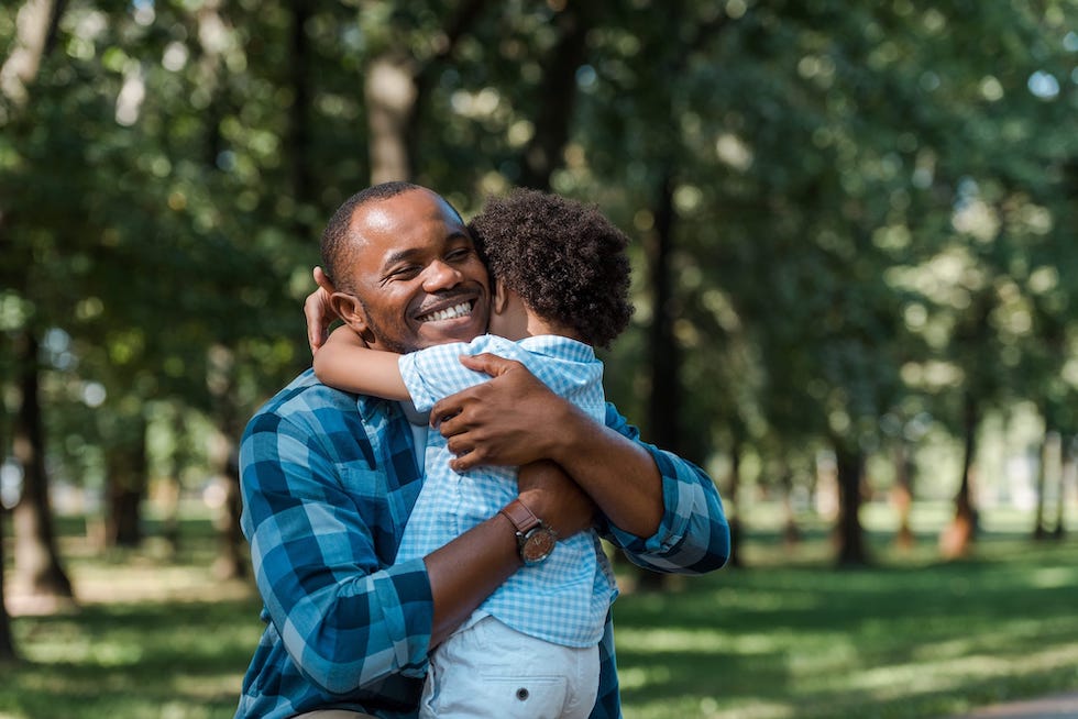 Un père heureux serre dans ses bras son fils qui porte une chemise à carreaux.