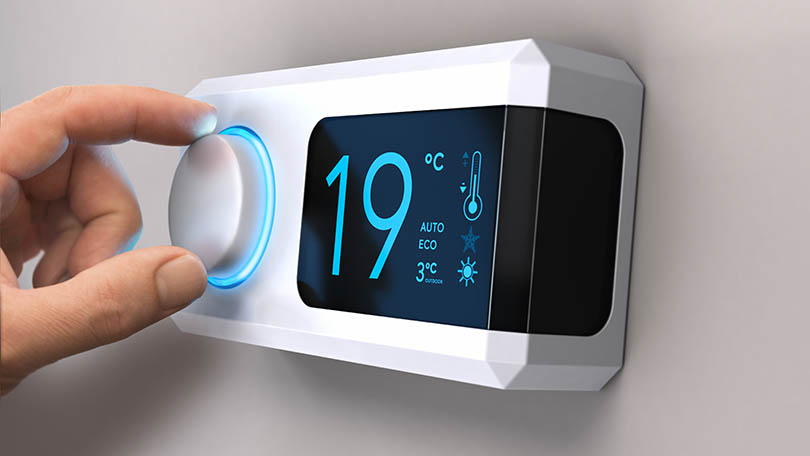 Personne ajustant un thermostat numérique, qui indique 19 degrée Celsius.