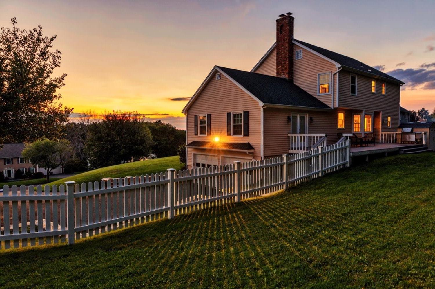 L'arrière d'une maison avec un porche arrière, un barbecue et une clôture blanche, au coucher du soleil. 