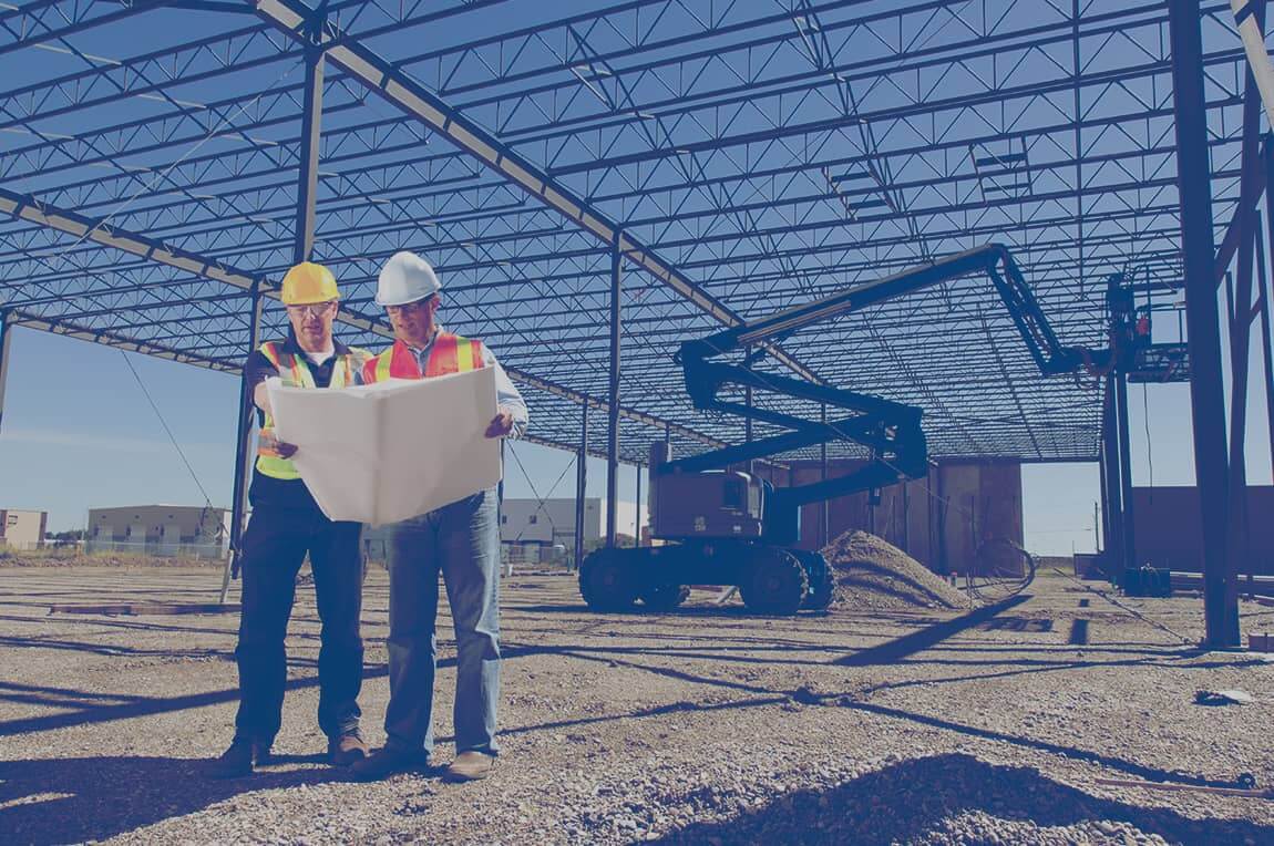 Deux travailleurs de la consutruction examinant un plan sur le chantier d'un bâtiment commercial.