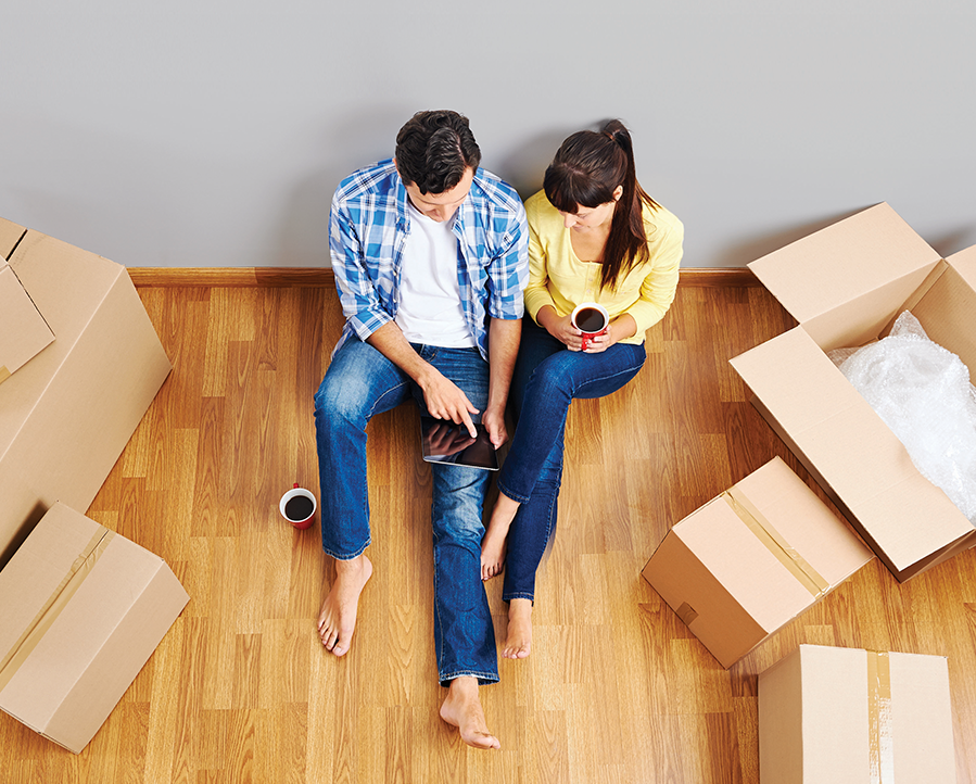 Couple se préparant à déménager avec des boîtes autour de lui. Ils boivent un café et regardent une tablette.