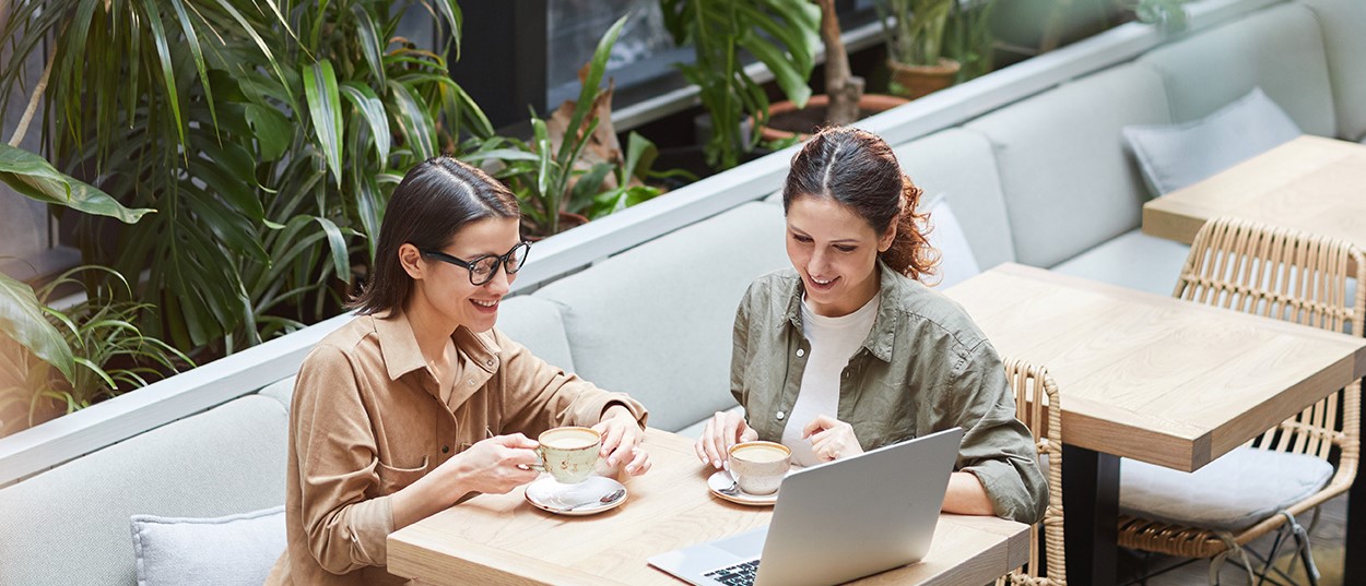 Deux femmes regardant l'écran de leur ordinateur portable tout en dégustant un café dans un café.