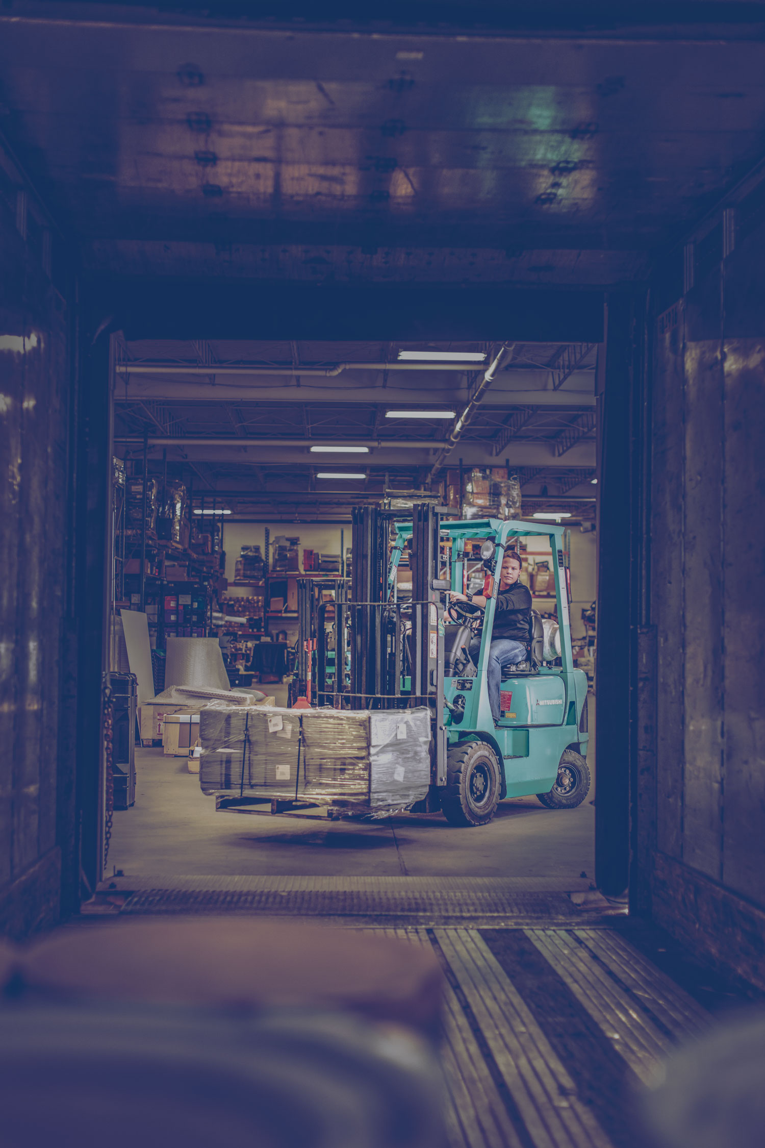 Un chariot à fourche au propane dans un entrepôt. Il remplit une remorque de palettes de produits.