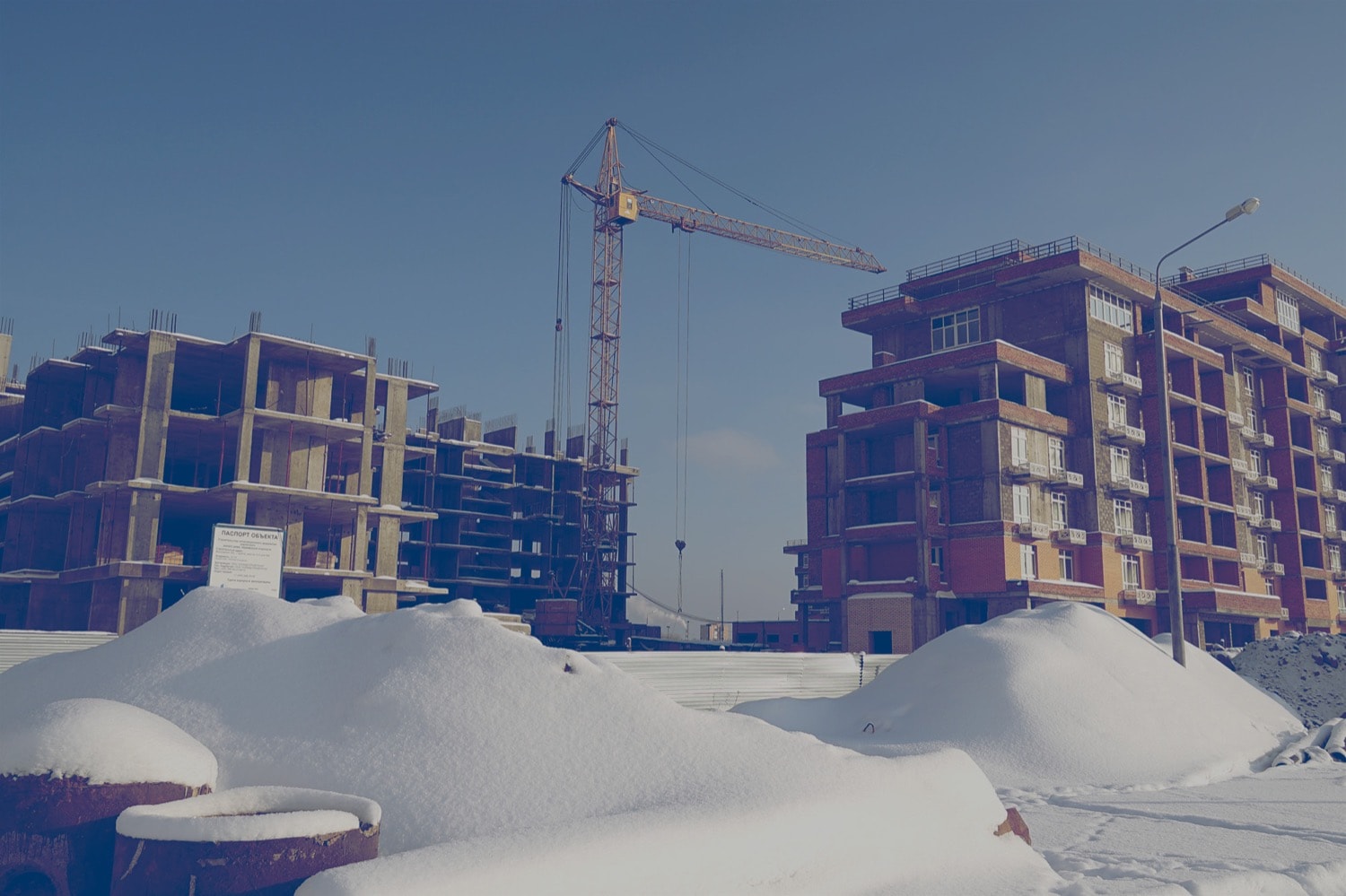 Deux condos en construction avec une grue en arrière-plan et de la neige au sol.
