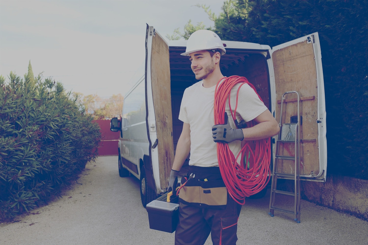 Un travailleur de la construction portant un casque blanc transporte ses outils de sa fourgonnette au chantier.