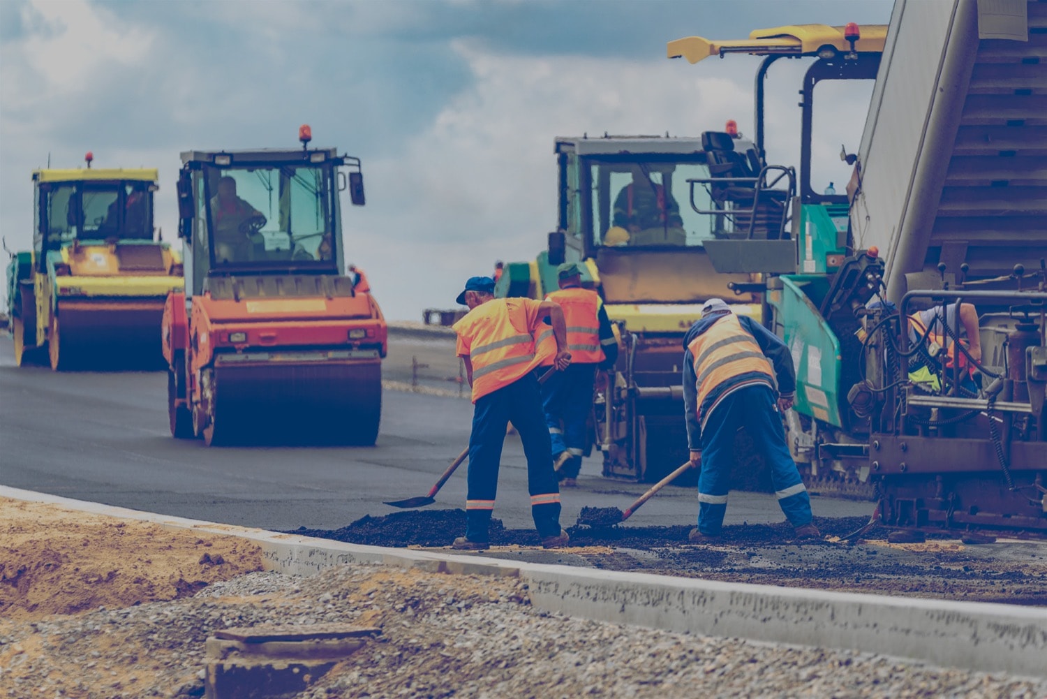 Une équipe épand de l’asphalte sur une route et des rouleaux compresseurs le lissent.