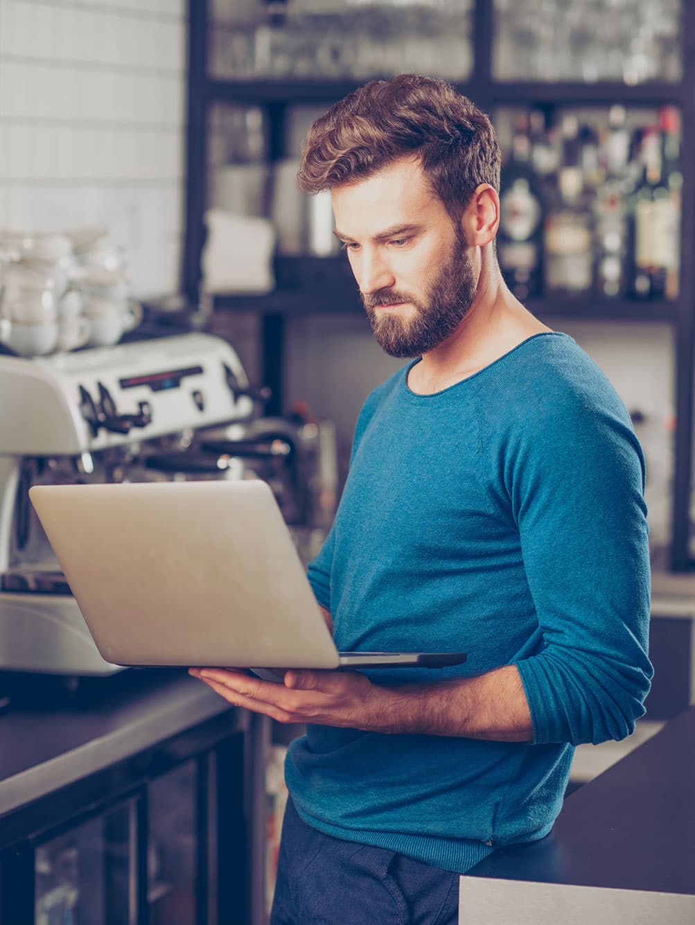 Une barista regarde l’écran d’un ordinateur portable près d’une machine à espresso.