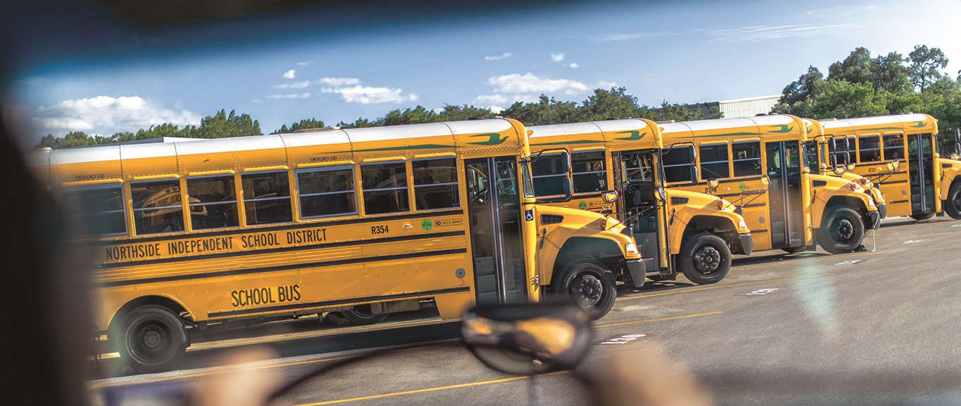Photo prise par-dessus l'épaule d'un chauffeur de bus conduisant avec des bus scolaires au propane devant lui
