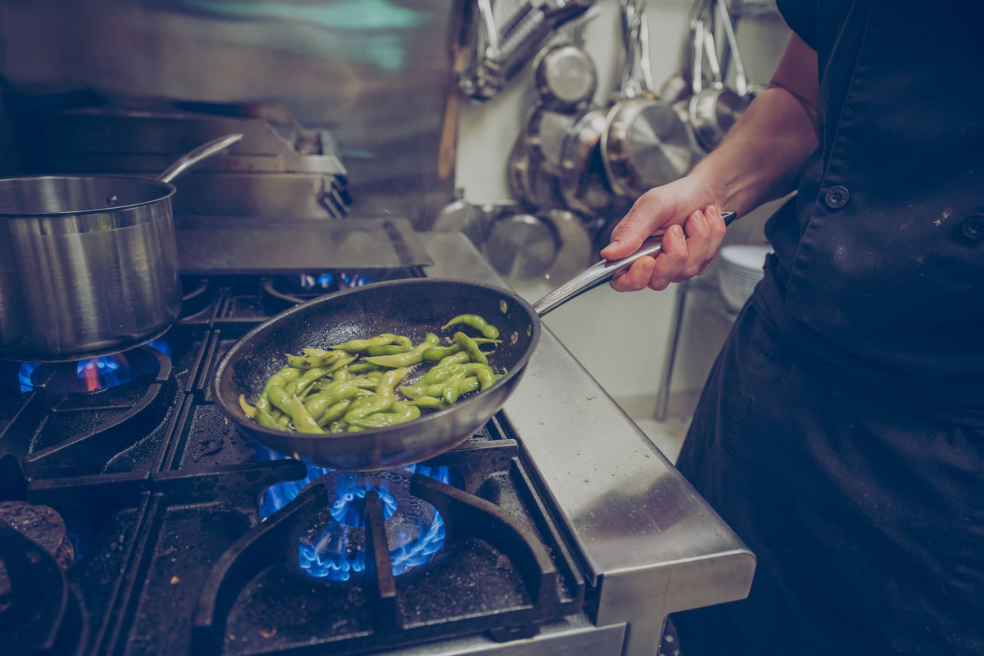 Un chef fait cuire des edamames dans une poêle à frire sur une cuisinière au propane.