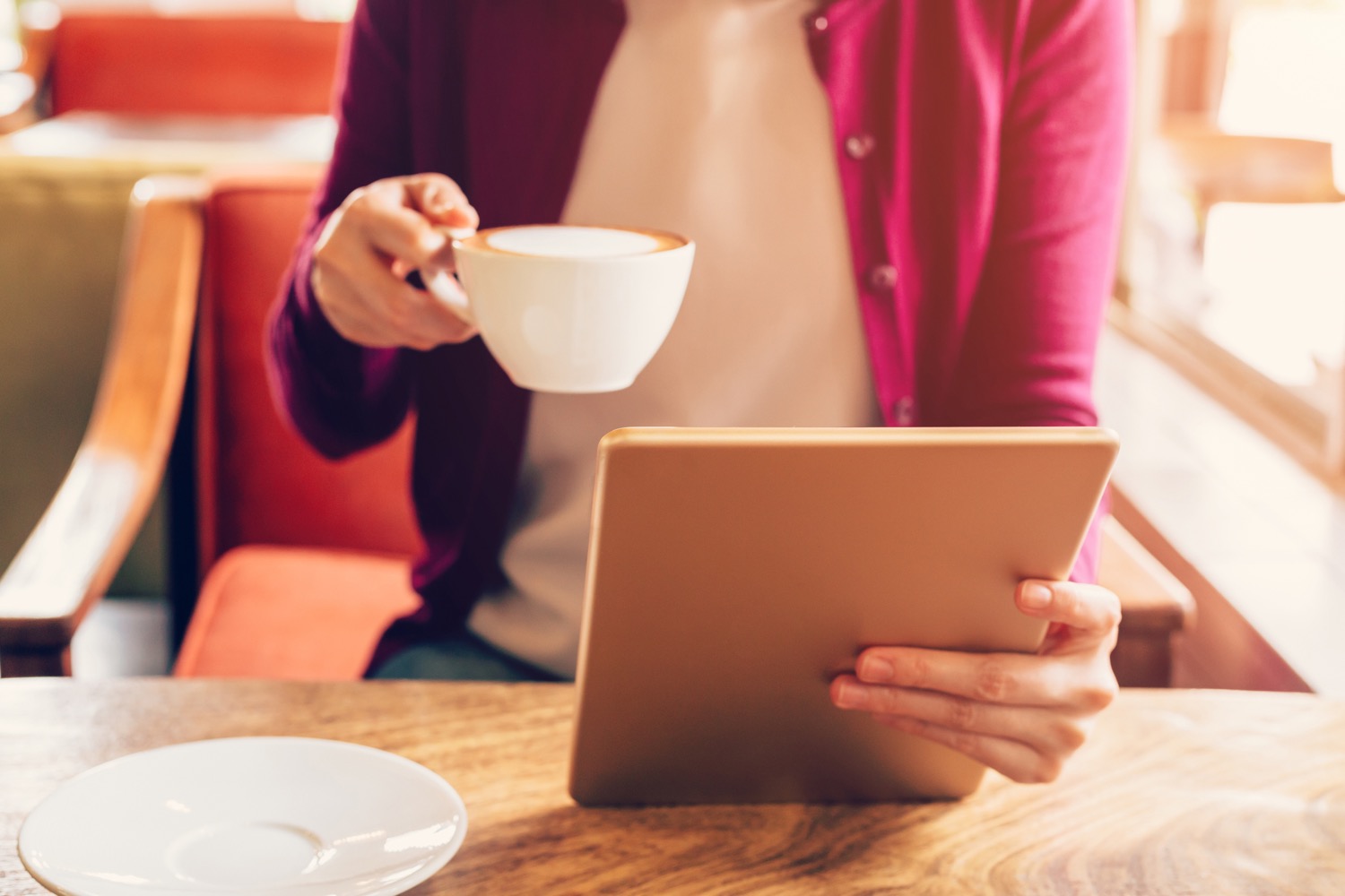 Femme tenant un latté tandis qu'elle regarde une tablette, dans un café.