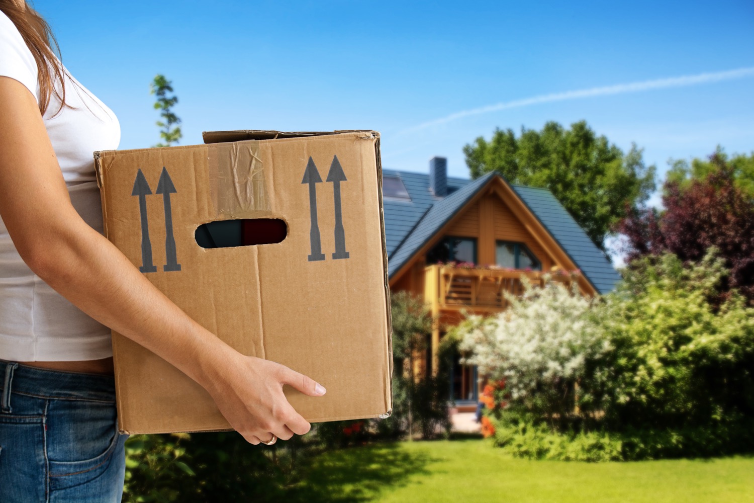 Femme tenant une boîte de carton devant une maison.