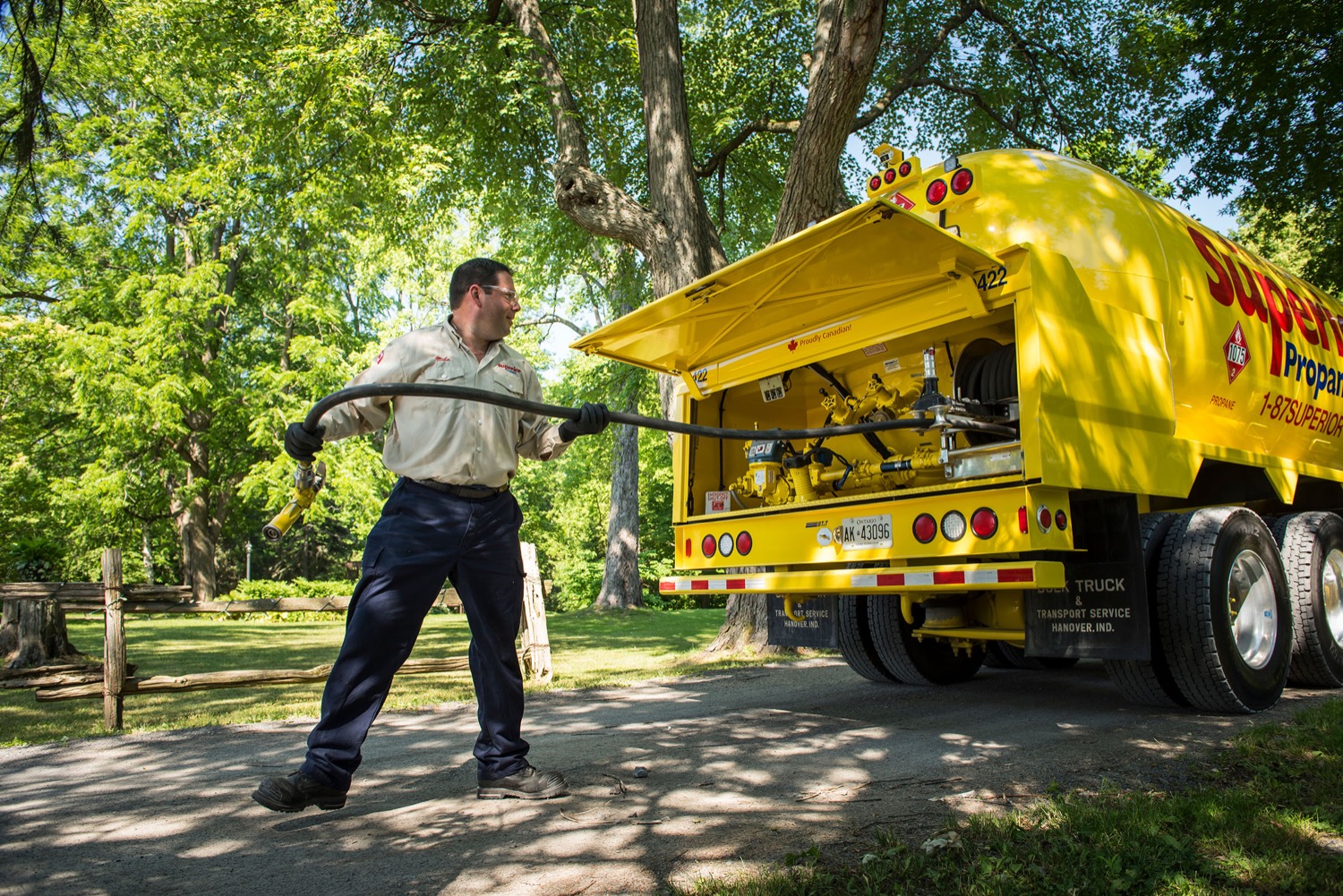 Employé de Supérieur Propane tirant une conduite de gaz, de l'arrière de son camion et marchant sur une route de terre.