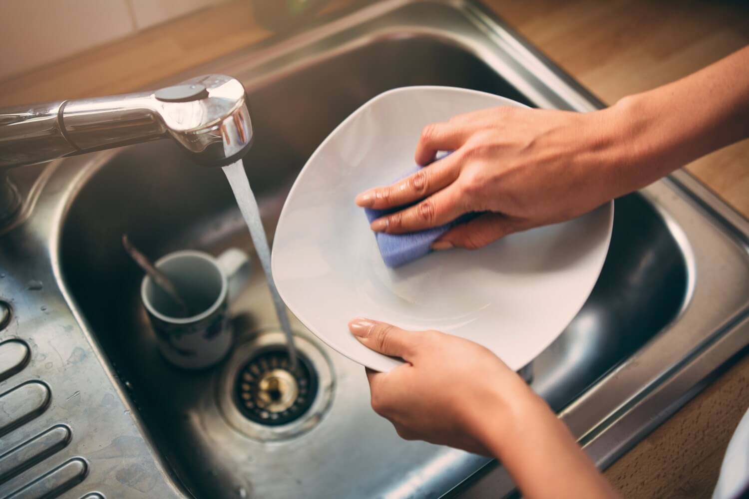 Personne nettoyant une assiette blanche dans un évier à l'aide d'une éponge bleue. L'eau s'écoule et est chauffée au propane.