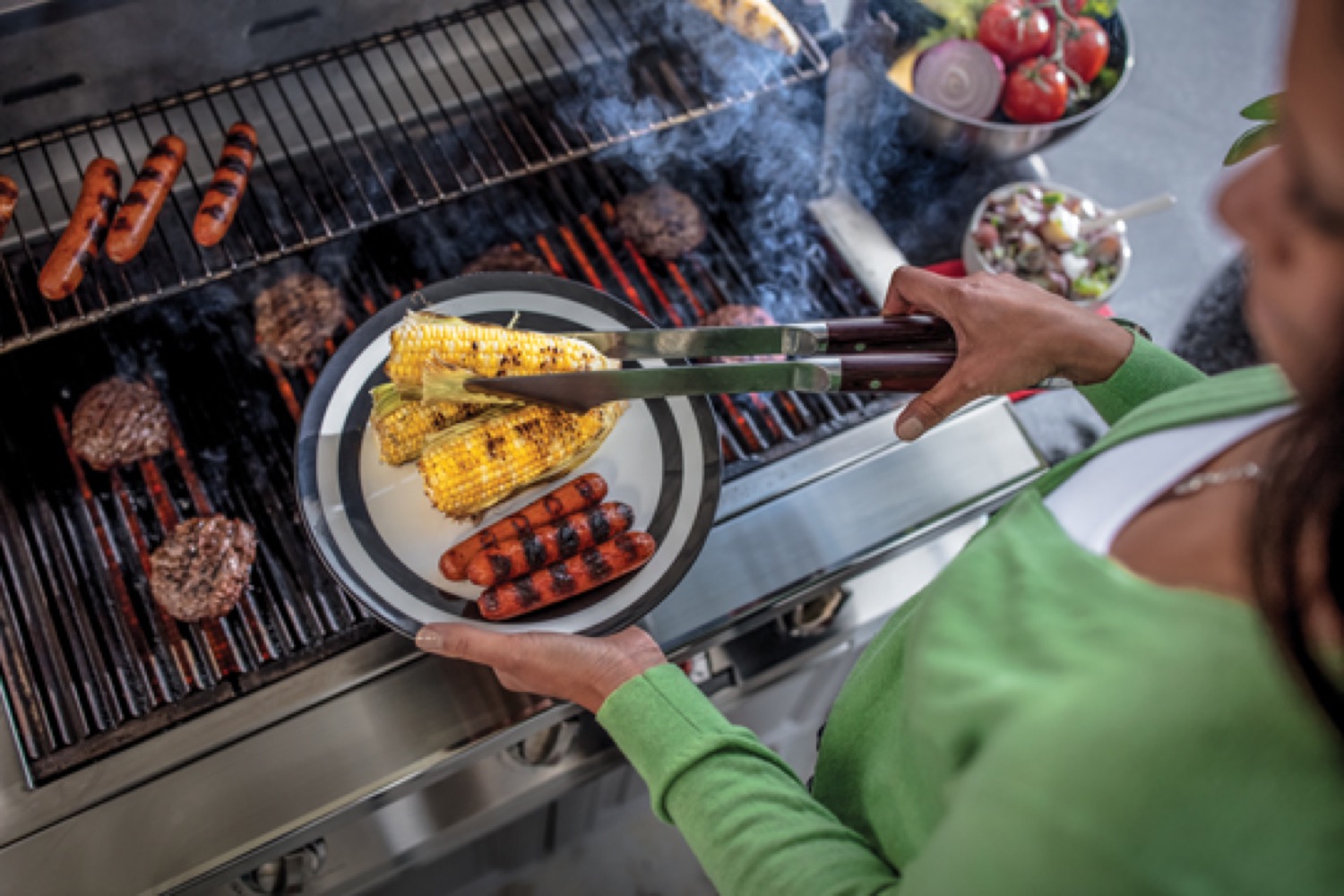 Femme retirant maïs et hot-dogs d'un barbecue au propane et qui les place sur une assiette.