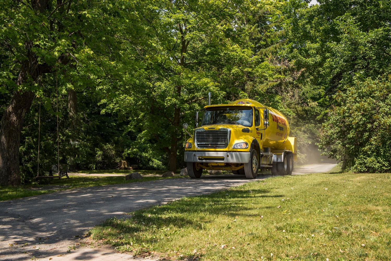 Camion Supérieur Propane effectuant une livraison à une maison sur un chemin de terre rural bordé d'arbres.
