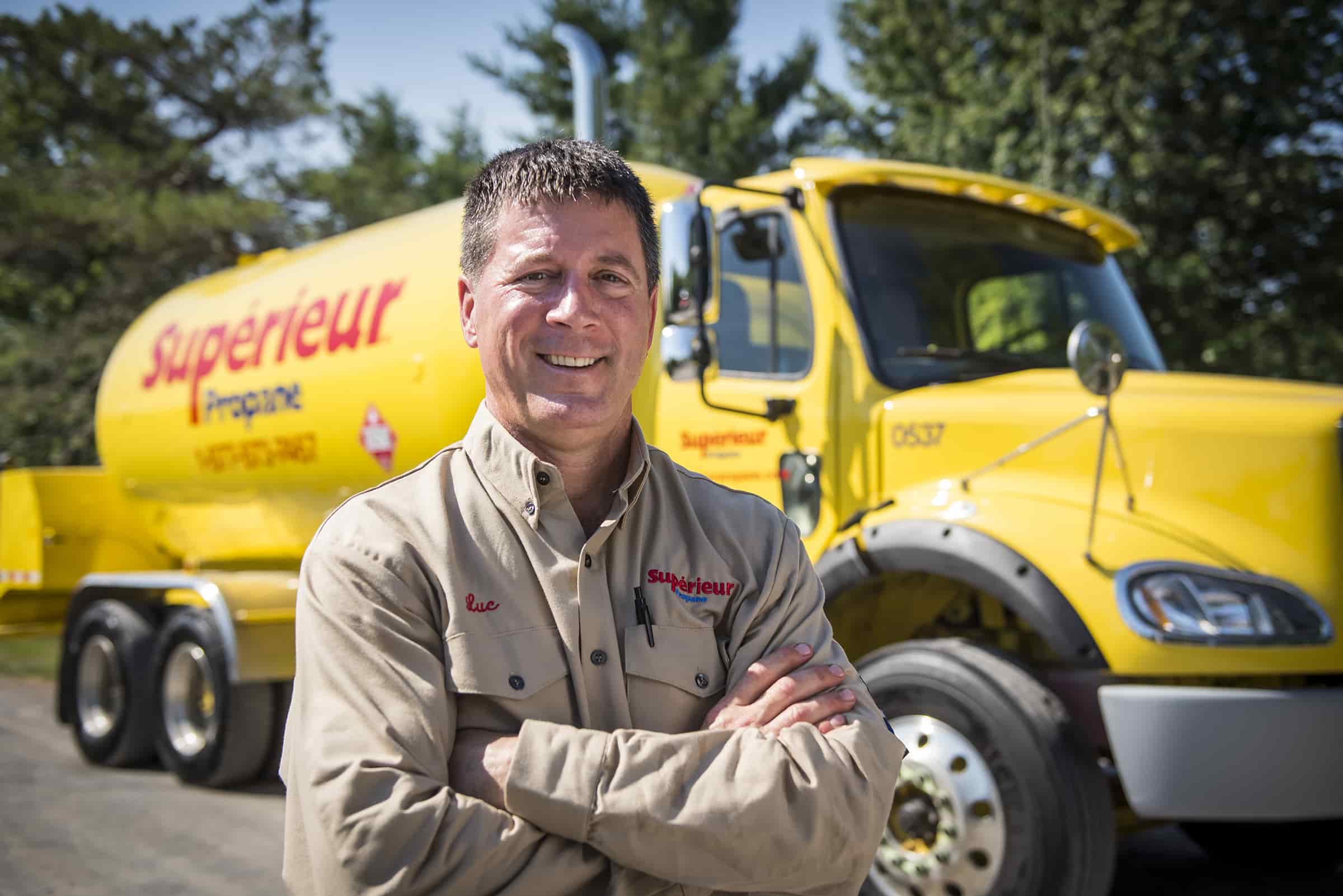 Le livreur de Supérieur Propane, joyeux, se tient devant son camion jaune.