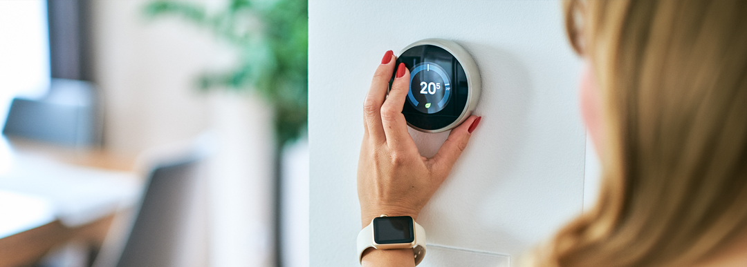 une Femme vérifiant le thermostat de la maison